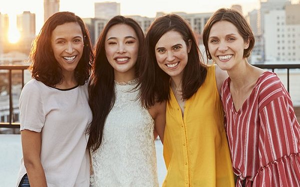 Portrait Of Female Friends Gathered On Rooftop Terrace For Party With City Skyline In Background