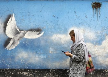 Iranian woman walks past a wall painting of peace bird in a street in downtown of Tehran, Iran. EPA-EFE/ABEDIN TAHERKENAREH